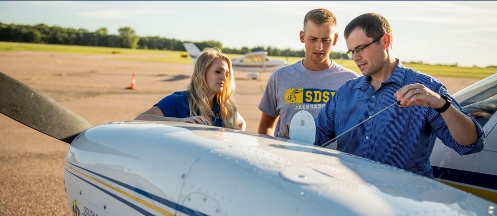 Two students and professor standing next to a plane.